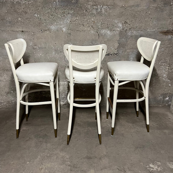 Off-white, mid-century bentwood barstools with upholstered seats and cane back rests.