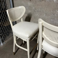 Off-white, mid-century bentwood barstools with upholstered seats and cane back rests.