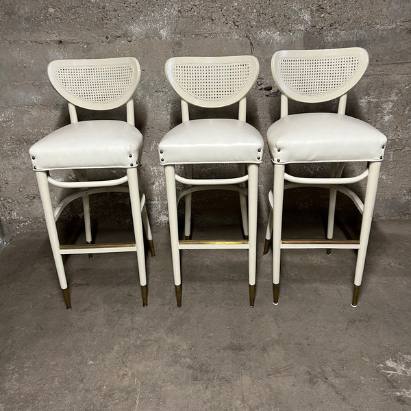 Off-white, mid-century bentwood barstools with upholstered seats and cane back rests.