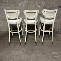 Off-white, mid-century bentwood barstools with upholstered seats and cane back rests.